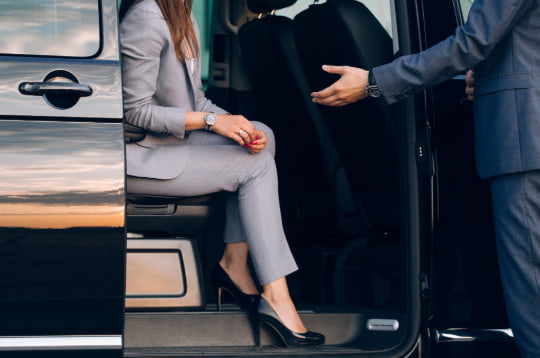A chauffeur opens the door of a sprinter van for a passenger in a suit